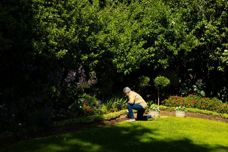 side-view-biracial-senior-woman-with-short-hair-gardening-while-kneeling-grassy-land-yard_13339-307404